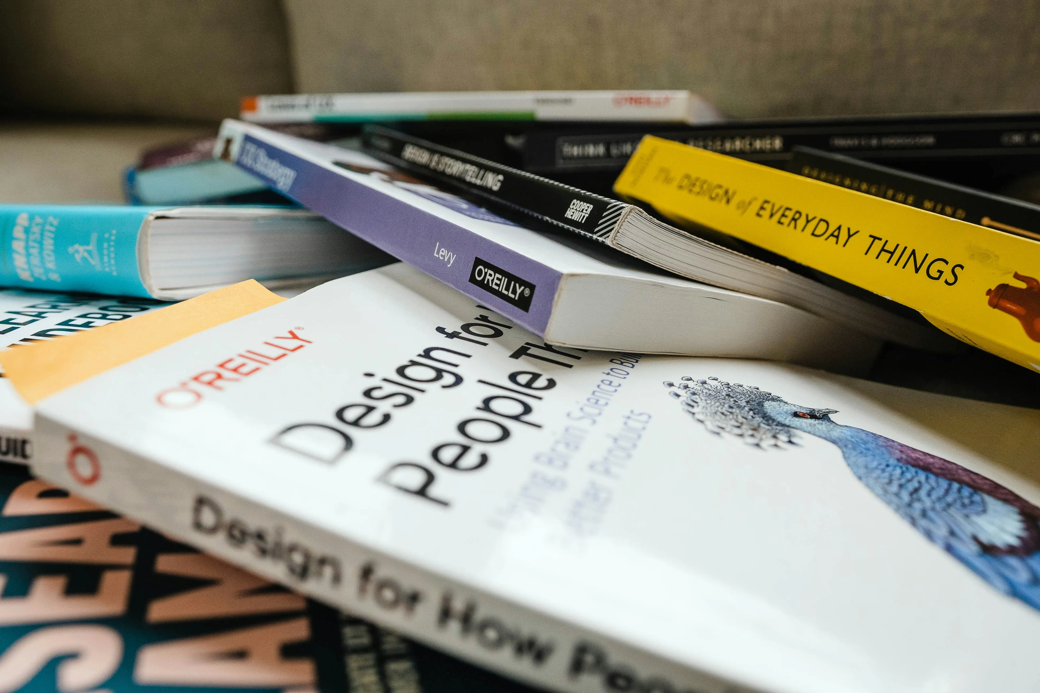 O stivă de cărți groase de design grafic și branding, așezate pe o masă de lucru, sugerând procesul de cercetare și studiu din spatele unui logo profesionist.