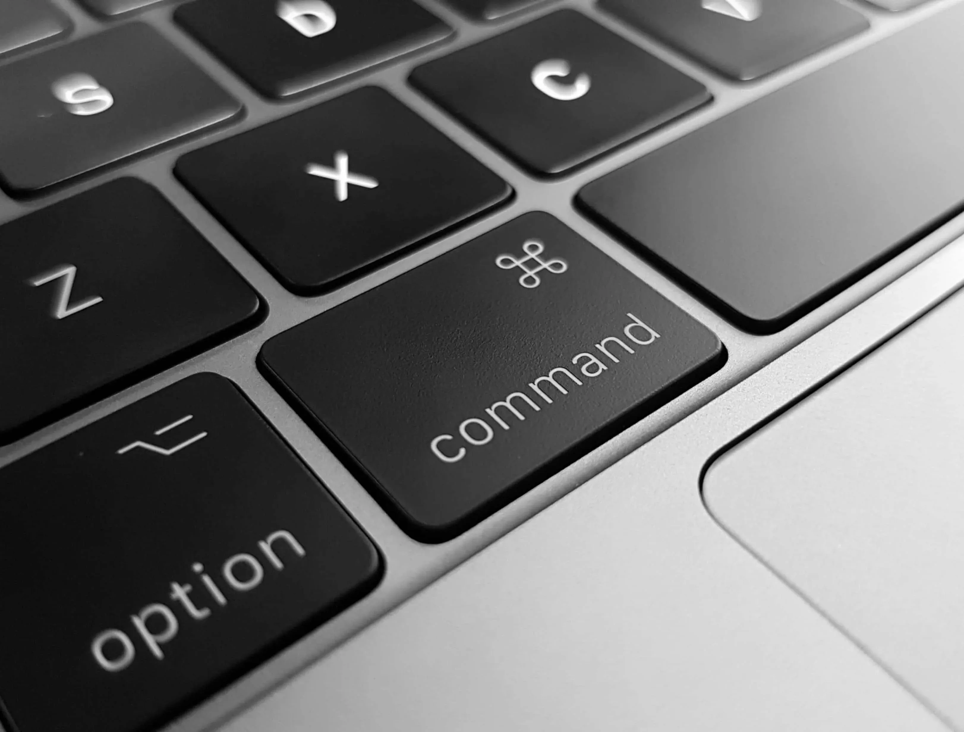 Closeup al unei tastaturi negre de Mac cu backlight, focalizată pe butonul Command, simbolizând controlul și acțiunea în înregistrarea unui domeniu de Internet.